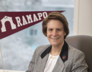 Dr. Cindy Jebb smiling in her office with Ramapo College banner behind her desk.